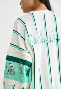 Λευκή μπλούζα με μακρύ μανίκι και τιρκουάζ ρίγες, που διαθέτει κεντημένο λογότυπο "ADIDAS ORIGINALS" και εκτυπωμένα γραφικά με μπολέρ στο μανίκι.