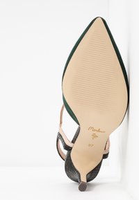 Chaussure à talon haut avec un bout pointu, tige en daim vert, côtés en cuir noir texturé et accents beiges. Présente un talon fin et une semelle texturée.