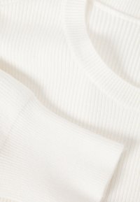 Tissu blanc côtelé présentant de fines lignes verticales, avec un col rond et un détail de manche longue à revers. La texture douce est évidente.