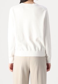 Bílý bavlněný svetr s žebrovanými manžetami a pasem, s kulatým výstřihem a hladkou texturou,nošený s béžovými širokými kalhotami.