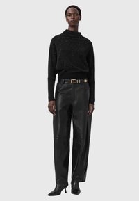 Schwarzer glitzernder Pullover mit hohem Kragen, kombiniert mit lockeren schwarzen Lederhosen. Akzentuiert mit einem breiten Gürtel mit goldener Schnalle.