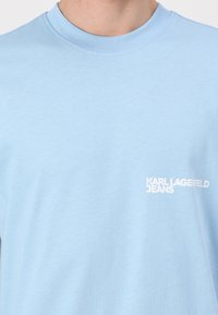Világoskék kereknyakú póló fehér "KARL LAGERFELD JEANS" logóval a bal mellrészen.