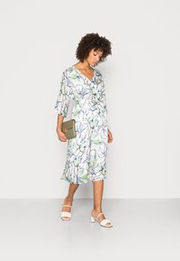 Vestido envolvente floral com padrões azul claro e verde em tecido branco, até ao joelho, com mangas três quartos e um laço na cintura.