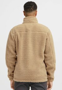 Pullover in pile beige con colletto alto e esterno testurizzato. Presenta una vestibilità comoda e dettagli di cucitura sulle spalle e sulla schiena.