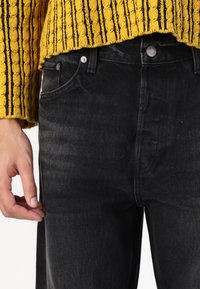 Czarne jeansy z denimu o prostym kroju, pięcioma kieszeniami, srebrnymi elementami i subtelną fakturą. Połączone z żółtym, dzianinowym swetrem.