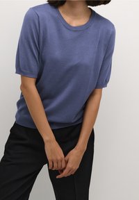 Kortærmet, rundhalset pullover i blødt, lyseblåt stof. Enkel design med ribbede manchetter, bæres med mørke bukser.