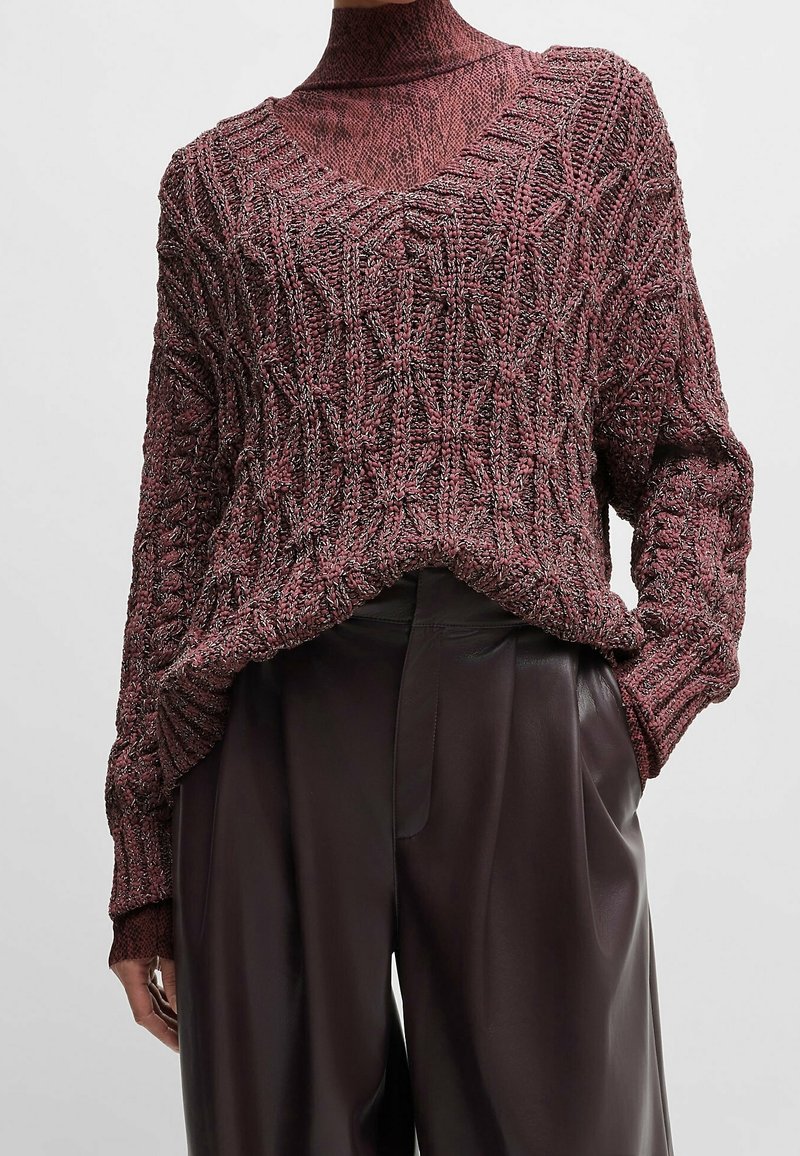 Pull en maille bordeaux avec col en V, motif texturé et épaules tombantes, associé à un pantalon en cuir noir taille haute.