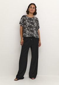 Black and white patterned short-sleeve top paired with loose black pants. The top features a round neckline and relaxed fit.