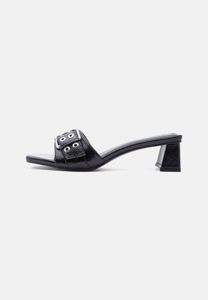 Black open-toe mule with low block heel and wide strap featuring silver buckle and eyelet details, shown in side view.