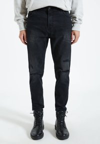 Czarne zniszczone dżinsy o slim fit, z wycięciami na kolanach i wysokim stanem, zestawione z czarnymi skórzanymi botkami na sznurówki.