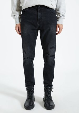 Svart slitna jeans med slim fit, med revor vid knäna och hög midja, kombinerade med svarta läderstövlar med snörning.