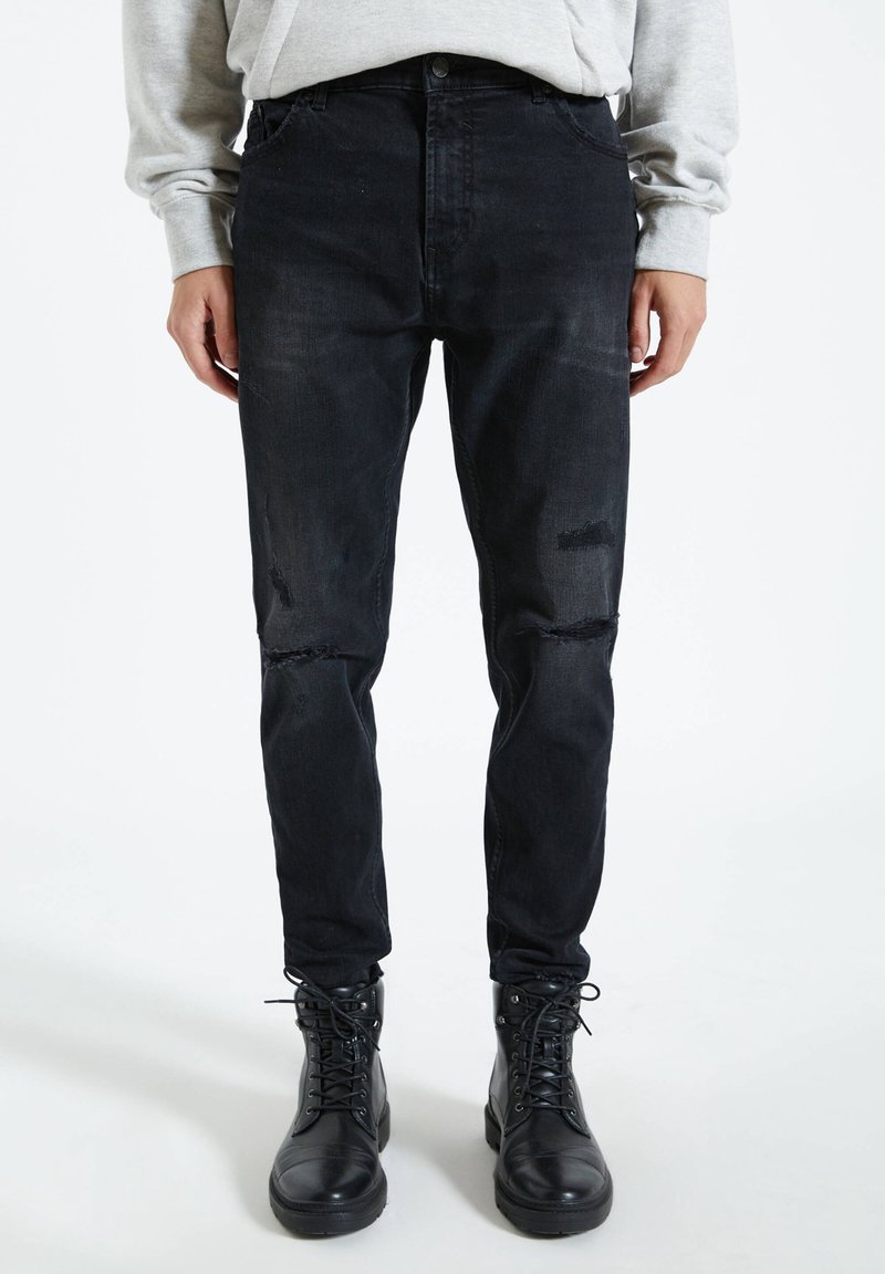 Czarne zniszczone dżinsy o slim fit, z wycięciami na kolanach i wysokim stanem, zestawione z czarnymi skórzanymi botkami na sznurówki.