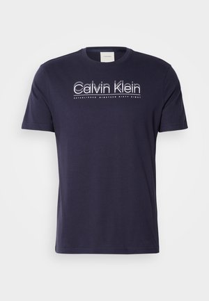 T-shirt in cotone blu navy con maniche corte, collo tondo e logo bianco di Calvin Klein con "FONDATO NEL MILNOVESESANTOTTO" sotto.