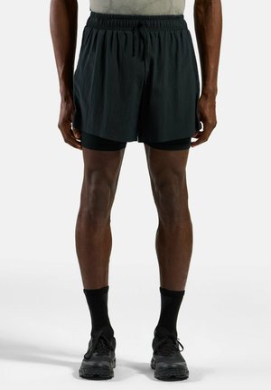Schwarze Shorts mit elastischem Bund und Kordelzug. Tragen über schwarzen enganliegenden Shorts, kombiniert mit schwarzen Socken und Turnschuhen.