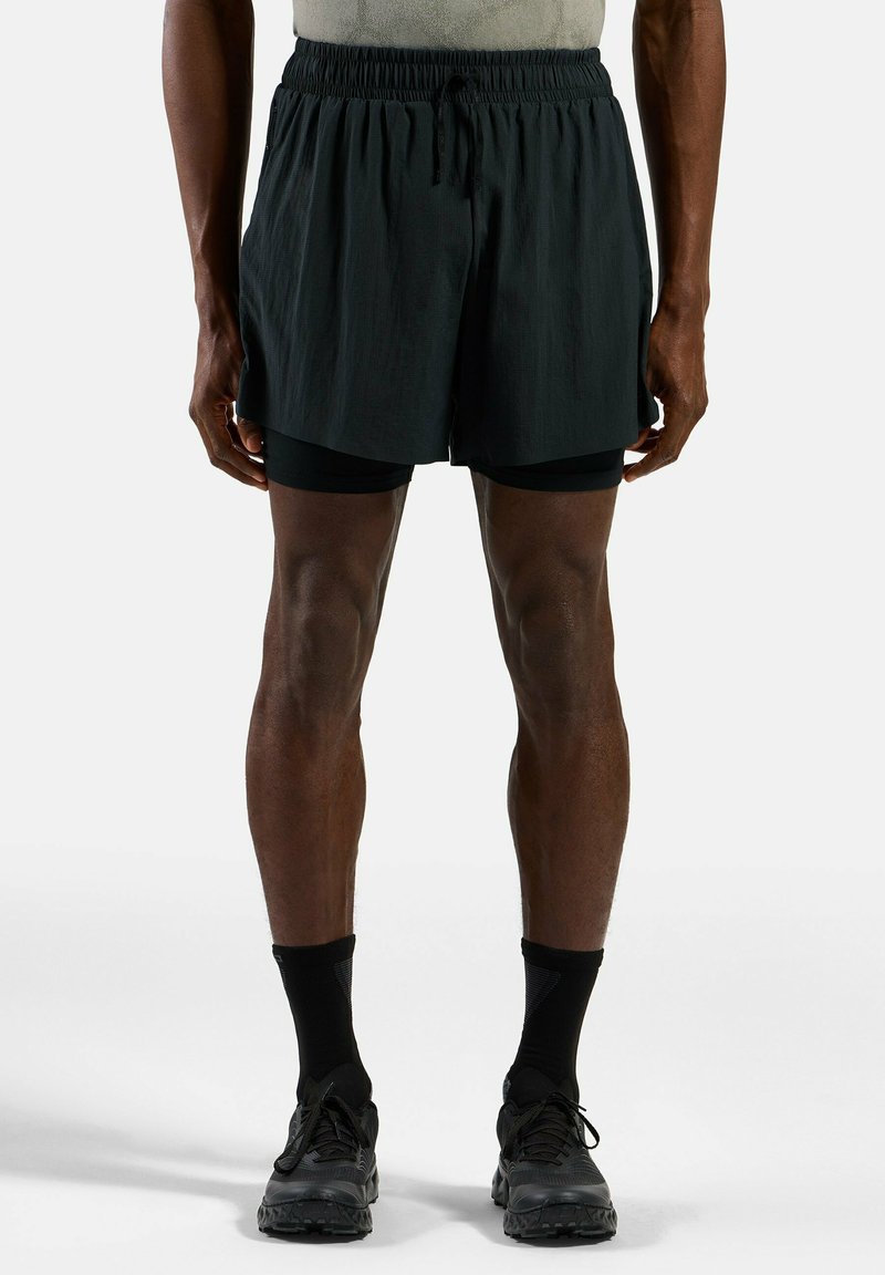 Zwarte shorts met een elastische tailleband en trekkoord. Draag over zwarte strakke shorts, gecombineerd met zwarte sokken en sneakers.