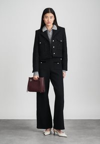 Svart cropped jakke med gullknapper og to lommer foran, kombinert med høytlivede svarte bukser. Hvite sko og en burgunder teksturert håndveske.