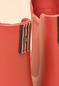 Stivali di gomma color corallo con finitura strutturata, caratterizzati da un dettaglio in tessuto a righe multicolori e un logo metallico sul lato.