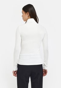 Hvid langærmet turtleneck bluse lavet af ribbet stof, med en tætsiddende silhuet og sømløs design, parret med sorte bukser.