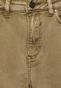 Pantalones vaqueros de mezclilla verde oliva con un bolsillo frontal, cierre de botón de metal y detalles cosidos a lo largo de las costuras. Textura suave.