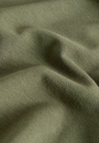 Gros plan sur un tissu vert avec une texture fine côtelée et des plis doux créant des ombres et des reflets.