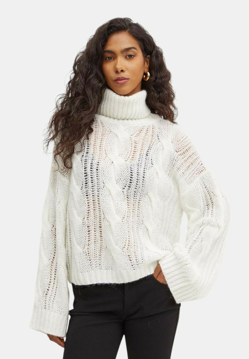 Maglione bianco a collo alto, lavorato a maglia, con motivo a trecce e trama aperta. Presenta maniche ampie e una vestibilità corta, indossato con pantaloni neri.
