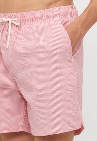 Κόκκινες και λευκές ριγέ μαγιό από ελαφρύ ύφασμα, με ρυθ�μιζόμενη μέση με κορδόνι και πλαϊνές τσέπες.