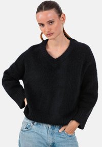 Schwarzer, übergroßer V-Ausschnitt-Pullover aus weichem, strukturiertem Stoff mit langen Ärmeln und gerippten Bündchen, kombiniert mit hellblauen Jeans.