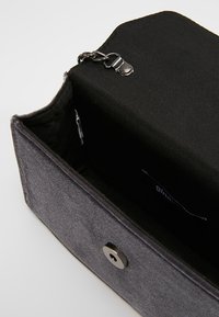 Borsetta in tessuto nero con chiusura a scatto metallica, che mostra un interno foderato e un dettaglio a catena sul bordo superiore. Design rettangolare semplice.