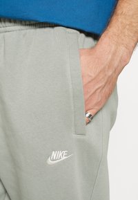 Hellgraue Sweatpants mit weicher Textur, elastischem Bund, seitlichen Taschen und einem weißen gestickten Nike-Logo.