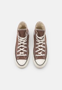 Zapatillas altas de lona marrón con cordones blancos, puntera de goma y detalle de costura en contraste. Presentan suela negra y parche de logo.