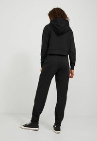 Black cropped hoodie with a hood paired with matching joggers. Material appears soft with elastic cuffs and waistband. Converse shoes complete the look.