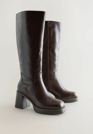 Botine din piele maro, până la genunchi, cu vârf rotund, toc pătrat și fermoar lateral. Textură netedă cu detalii subtile de cusătură.