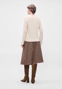 Μπεζ υφασμάτινος πουλόβερ με μακριά μανίκια, συνδυασμένο με καφέ φούστα μέχρι το γόνατο και καφέ σουέτ μπότες μέχρι το γόνατο με χρυσό κούμπωμα.