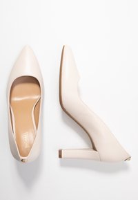 Escarpins beiges à bout pointu, finition en cuir lisse, petit talon bloc, et un design ouvert sur le côté avec un accent doré.