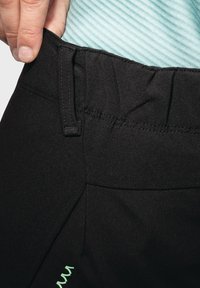 Schwarze Sporthosen mit glatter Textur, elastischem Bund und einem mintgrünen Akzent an der Seite. Nahaufnahme des Bunddetails.