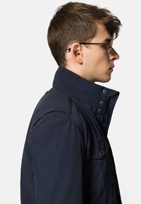 Granatowa kurtka puchowa z wysokim kołnierzem, zatrzaskami i bocznymi kieszeniami; gładka tekstura o lekko błyszczącym wykończeniu.