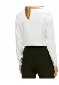 Blusa blanca de manga larga con corte recto y escote redondeado, combinada con pantalones negros de corte recto con bolsillos traseros.