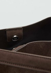 Brown suede handbag interior with a magnetic snap closure, featuring a smooth texture and a subtle brand logo embossed.