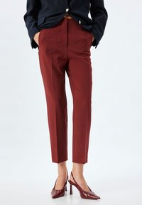 Burgundy tailored trousers with a high waist, sharp creases, and a slim fit, paired with glossy pointed-toe heels in a matching color.