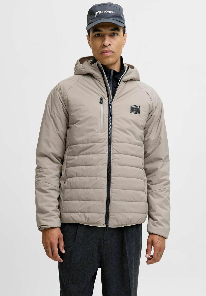 Beige gepolsterte Jacke mit einem Reißverschluss auf der Vorderseite, normaler Passform und Kapuze. Verfügt über eine kleine Brusttasche und kontrastiert mit einem schwarzen Innenfutter.