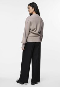 Pull en tricot marron clair avec des manches bouffantes, associé à un pantalon large noir. Poignets et ourlet côtelés visibles. Texture lisse.