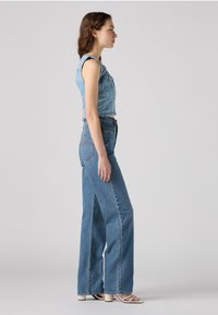 Veste cropped en denim avec fermeture à boutons, associée à un jean large taille haute avec fentes sur les côtés. Couleur bleu clair avec des coutures subtiles.