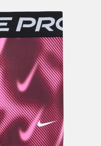 Fekete és rózsaszín Nike Pro anyagú rövidnadrág, átlós csíkokkal, sima textúrával és fehér Nike logóval a jobb alsó részen.