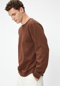 Brązowy sweatshirt z okrągłym dekoltem i długimi rękawami, wykonany z miękkiego materiału. Posiada luźny krój oraz ściągacze przy rękawach i u dołu.