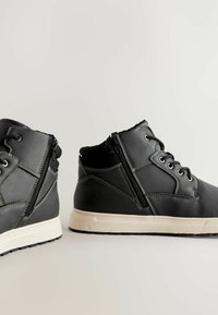 Schwarze High-Top-Schuhe aus synthetischem Leder mit einem Reißverschlussverschluss, weißen kontrastierenden Nähten und einer Gummisohle mit strukturiertem Profil.