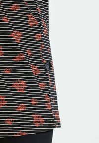 Camiseta de rayas en blanco y negro con patrones florales rojos. La tela es suave, con un detalle en el dobladillo y una pequeña etiqueta en el costado.