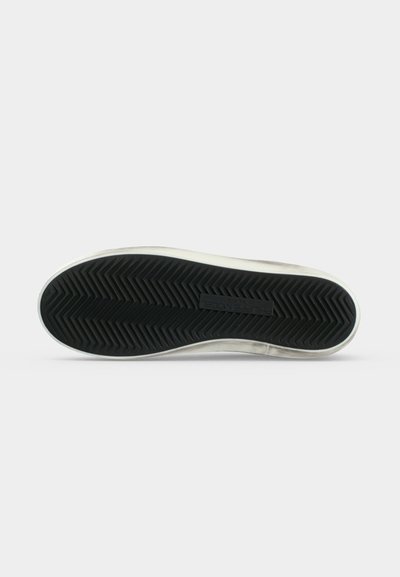 Semelle de chaussure en caoutchouc noire avec motif de semelle en zigzag, bord blanc et étiquette de marque rectangulaire visible près du centre.
