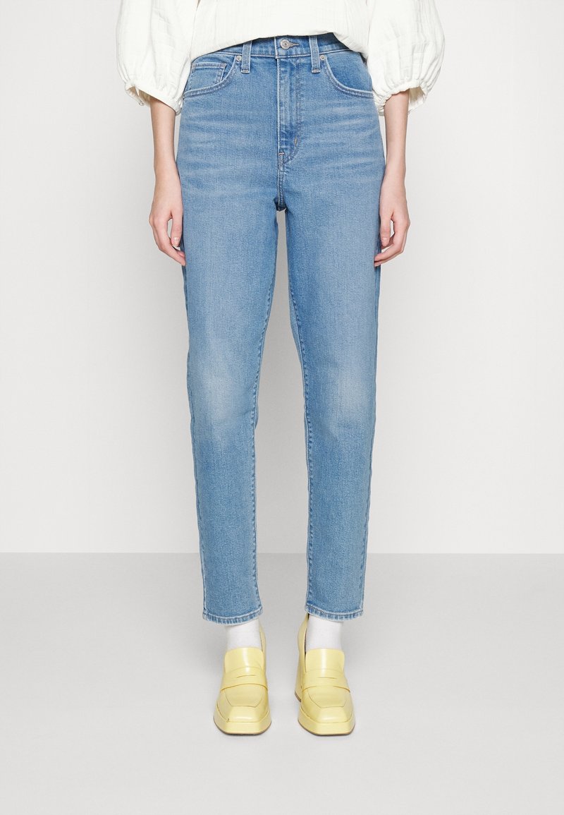 Jean taille haute bleu clair avec jambes droites. Portés avec des mocassins jaune clair. Texture en denim lisse et la tenue présente un design minimaliste.