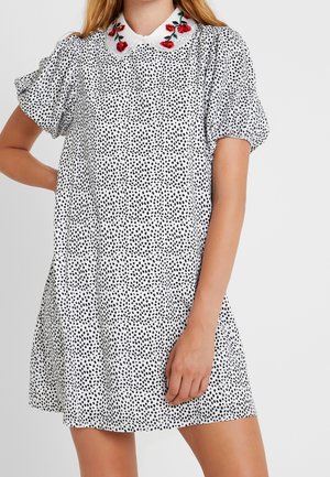 Svart och vit prickig klänning med korta puffärmar, krage med röd rosbroderi, och en avslappnad, utställd silhuett.