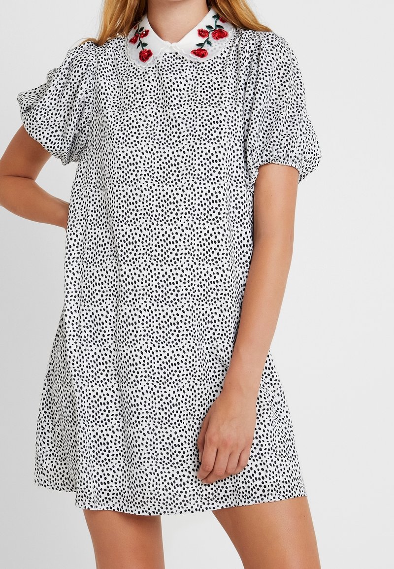 Black and white polka dot dress with short puff sleeves, collar featuring red rose embroidery, and a relaxed, flared silhouette.